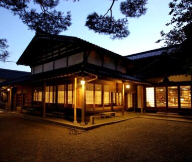 Evening view of wooden ryokan exterior with lit shoji windows and pine trees at Koshi no yado Takashimaya Niigata