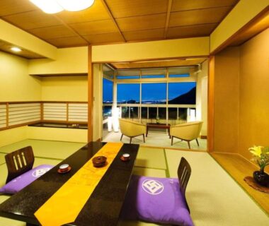 Tatami room with low dining table, purple floor cushions, sliding doors opening to balcony and distant evening sky, Kotobukitei Mie