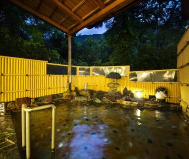 Stone outdoor onsen with bamboo fence and warm lantern lighting at Kotobukitei, Mie prefecture