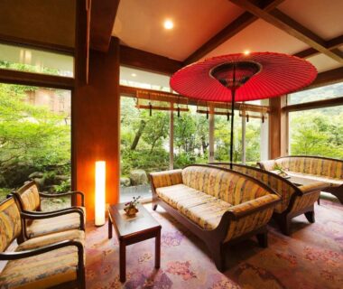 Traditional lounge with sofas, red parasol, wooden beams and garden views at Kotobukitei in Mie, Kansai, Japan