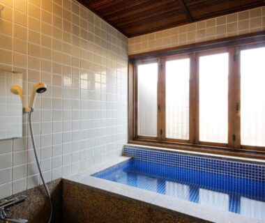 Blue-tiled indoor soaking tub with handheld shower and wooden framed windows at Kotonoyado Musashino Nara