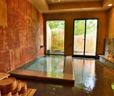 Indoor soaking tub with wooden buckets, tiled walls and garden-facing glass doors at Kotonoyado Musashino Nara