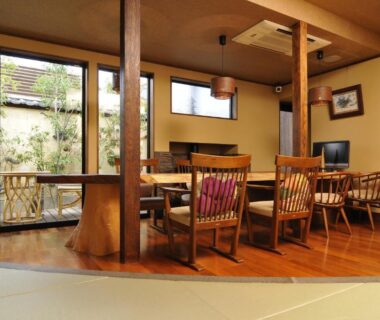 Interior with tatami floor, wooden dining table and chairs, sliding glass windows overlooking a garden at Kotonoyado Musashino in Nara