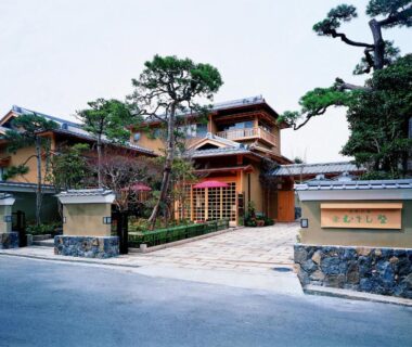 Entrance facade of Kotonoyado Musashino with wooden architecture, stone wall and pine trees in Nara Kansai