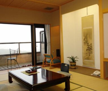 Tatami room with low table, tokonoma scroll, balcony chairs and distant water view at Kounkaku, Fukushima