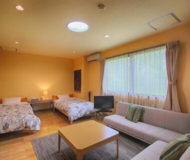 Warm twin room with beds, sofa, coffee table, TV and large curtained window at Kounso in Yamanashi