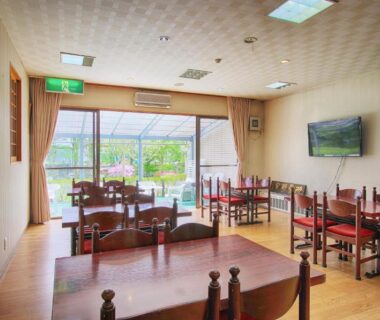Bright dining area with wooden tables and chairs and large windows overlooking garden at Kounso ryokan in Yamanashi