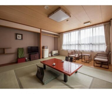 Tatami room with low red table, floor chairs, TV cabinet and large curtained window at Kouunsou in Tochigi