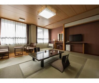 Spacious tatami room with low table, chairs, TV and large windows at Kouunsou in Tochigi