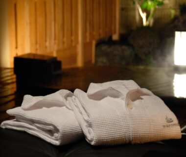 Folded white robes beside an indoor wooden onsen bath illuminated by soft lantern lighting