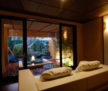 Seated tatami lounge with cushions overlooking a small Japanese garden through sliding glass at Kouyurou Ikawa, Shizuoka