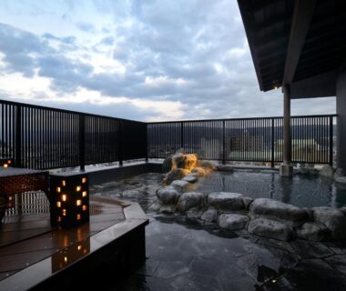 Outdoor stone onsen bath on wooden terrace with lanterns and distant mountain view at Kouyurou Ikawa Shizuoka