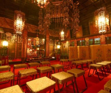 Temple hall with red carpet, cushioned stools, ornate hanging lanterns and altar at Koyasan Sanadabo Rengejoin, Wakayama