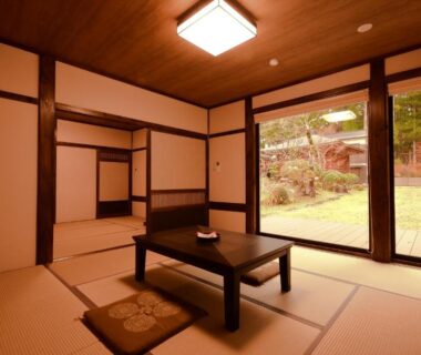 Traditional tatami room with low table, cushions and sliding doors opening to wooden deck and garden at Koyasan Shukubo Jokiin