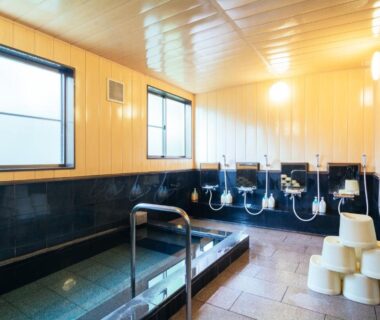 Bright indoor bath with tiled tub, shower stations and stools at Koyasan Shukubo Jokiin, Wakayama