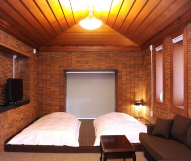 Twin futon beds on low platforms with wooden ceiling, sofa and TV at Kozuka Hisanoha, Kanagawa