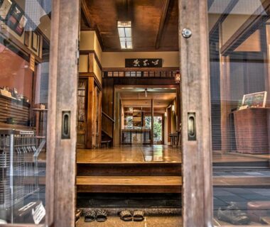 Wooden genkan entrance with glass doors, step and sandals at K's House Ito Onsen Shizuoka