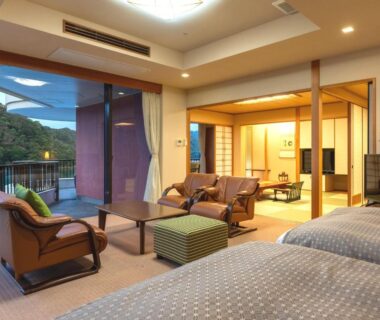 Spacious room with twin beds, tatami seating area, shoji screens and balcony overlooking wooded hills at Kumano-bettei Nakanoshima Wakayama
