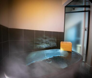 Steaming tiled indoor onsen bath with wooden bucket and frosted glass door at Kunisakisou Oita