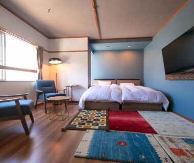 Bright room with twin beds, lounge chairs, wall TV and colorful rug at Kunisakisou in Ōita