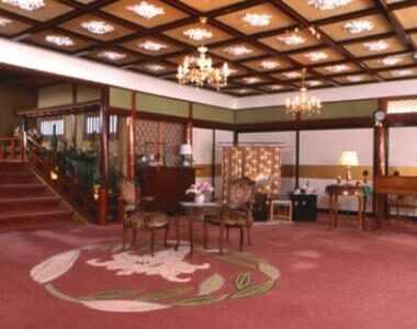 Spacious carpeted lobby with chandeliers, seating area, reception desk and wooden accents at Kurhaus Ishibashi in Shizuoka