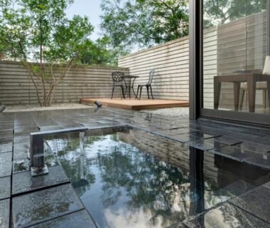 Stone tiled outdoor bath with wooden deck and patio chairs at Kurhouse Shirahama Wakayama