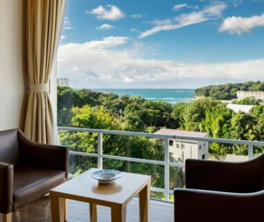 Balcony chairs and table overlooking the sea and coastal greenery at Kurhouse Shirahama, Wakayama