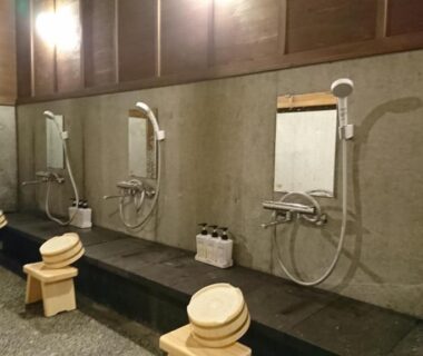 Communal washing area with wooden stools and handheld showers at Kurokawa Onsen Ryokan Ichinoi Kumamoto