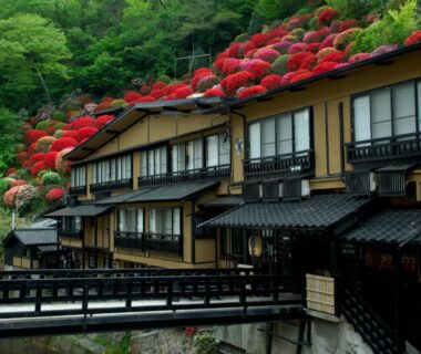 Wooden ryokan buildings along river with red azaleas, Kurokawa Onsen Yama no Yado Shinmeikan, Kumamoto, Kyushu