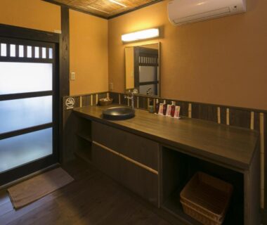 Wooden vanity area with basin, mirror, frosted sliding door and basket at Kurokawa-So ryokan in Kumamoto