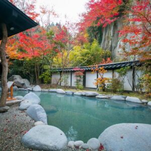 Outdoor onsen pool with red maple trees and stone edging at Kurokawa-So in Kumamoto, Kyushu