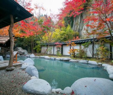 Outdoor onsen pool with red maple trees and stone edging at Kurokawa-So in Kumamoto, Kyushu