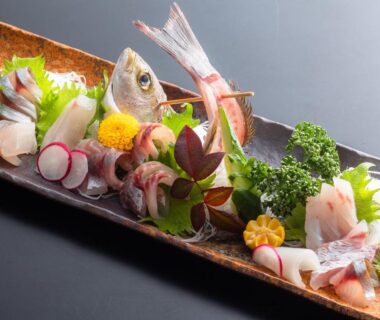 Assorted sashimi on a wooden platter with garnishes, radish slices and decorative leaves at Kurosakisou, Kyoto