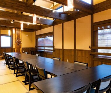 Long communal dining room with tatami flooring, wooden beams and low windows at Kurosakisou in Kyoto