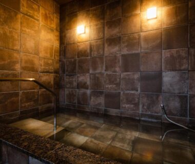 Tiled indoor onsen bath with warm wall lights and handrail at Kurosakisou Kyoto