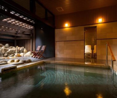 Warm indoor onsen bath at Kurotake with wooden walls, stone garden and reclining chairs, Nagano prefecture