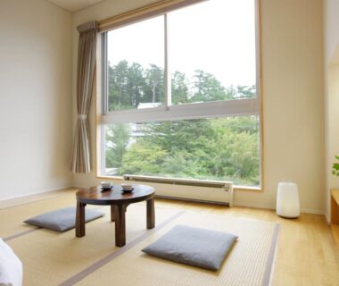 Minimal tatami room with low round table, cushions and large window overlooking tree-lined hillside