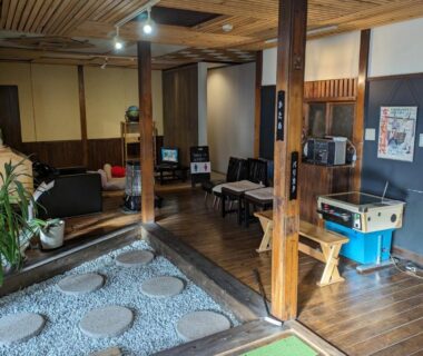 Wooden ryokan lounge with gravel courtyard, shoji screens, seating and retro game machine in Kusatsu Onsen Eidaya, Gunma
