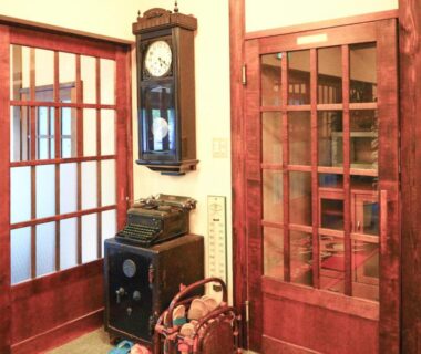 Foyer with wooden glass-panel doors, wall clock, vintage heater and basket at Kusatsu Onsen Eidaya, Gunma