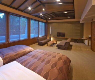 Twin beds with low lounge seating and large windows overlooking trees at Kusatsu Skyland Hotel in Gunma