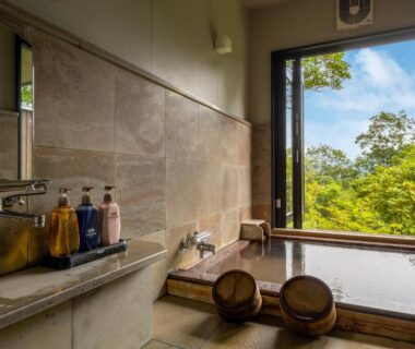 Indoor wooden onsen tub by window overlooking lush forest at Kusayane no yado Ryunohige, Ōita