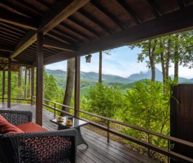 Wooden veranda with cushioned wicker chairs overlooking green mountains and forest at Kusayane no yado Ryunohige, Ōita