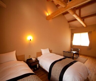 Warm twin-bedded room with exposed wooden beams, low table and soft lighting at Kutsurogi-no-Yado Nanakawa in Ōita