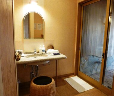 Washstand with mirror, wicker stool, toiletries and sliding door to bath area at Kutsurogi-no-Yado Nanakawa in Ōita