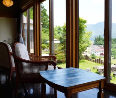 Wooden table and rattan chairs by large windows framing garden and distant mountains at Kutsurogian Niigata
