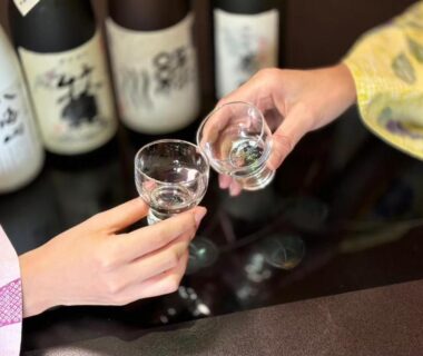 Two hands holding glass sake cups near bottles, yukata sleeve visible, Kutsurogian, Niigata, Chūbu Japan