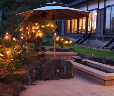 Wooden terrace with low benches, lantern string lights and shoji windows at Kutsurogian Niigata