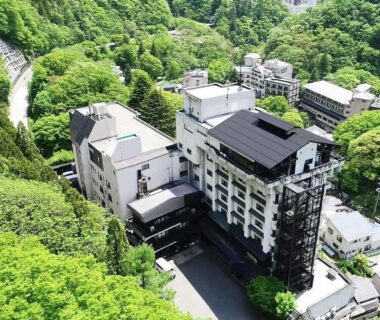 Multi-story ryokan building nestled in green forested valley with river and winding road, Kutsurogijuku Chiyotaki, Fukushima