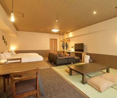 Spacious ryokan room with tatami area, low table with zabuton, western beds, sofa and TV at Kutsurogijyuku Shintaki