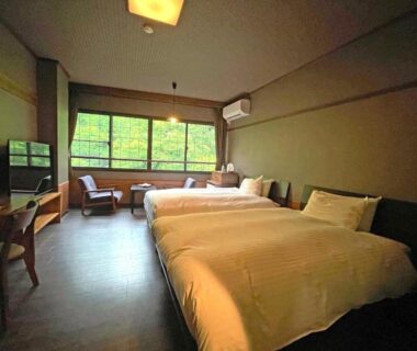 Twin beds with seating area and desk by large window overlooking greenery at Kutsurogijyuku Shintaki, Fukushima